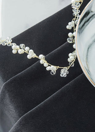 A delicate necklace with small pearls and clear crystal beads rests on a black fabric surface.