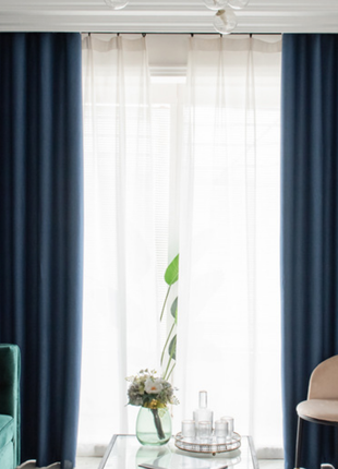 a modern living room with blue curtains, a green sofa, a glass coffee table, and a white chair.