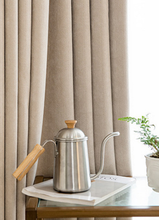 a silver kettle with a wooden handle, placed on a white tray, and a small potted plant next to it.