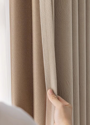 A hand is holding a beige curtain, examining it closely.