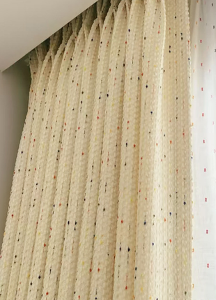 a close-up view of a beige curtain with multicolored dots, hanging from a rod.