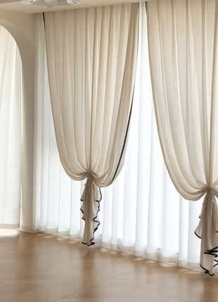 a room with three large, white curtains hanging from the ceiling. The curtains are tied back with black trim, creating a simple and elegant appearance. The room appears to be empty, with no other objects or furniture visible.