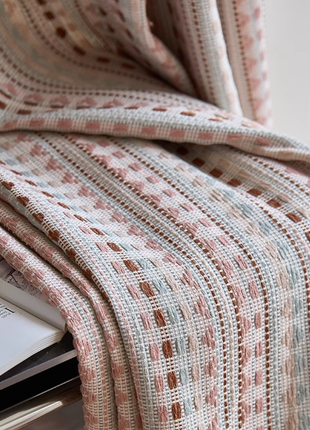 a close-up view of a woven fabric with a pattern of pink and white stripes, resting on a surface. There is also a small plate with a floral design visible in the image.
