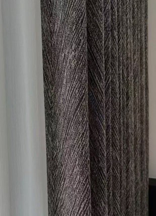 a close-up view of a dark-colored, textured fabric, possibly a curtain or textile, with a lighter fabric partially visible on the left side.