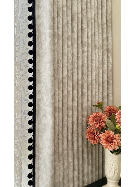 a white vase with pink flowers placed on a table, with a curtain featuring vertical lines and a black trim on the left side.