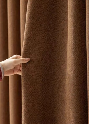A hand is holding a brown curtain, examining its texture and color.