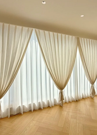a row of long, white curtains hanging from the ceiling, covering a large window with a wooden floor.