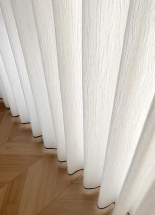 a close-up view of a white curtain with a wooden floor in the background.